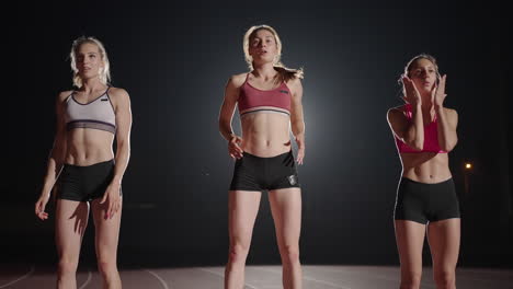 Three-women-athletes-prepare-for-a-track-race-in-a-dark-stadium-with-streetlights-on.-Time-lapse-footage-of-warm-up-and-concentration-of-a-group-of-women-before-the-race-on-the-track